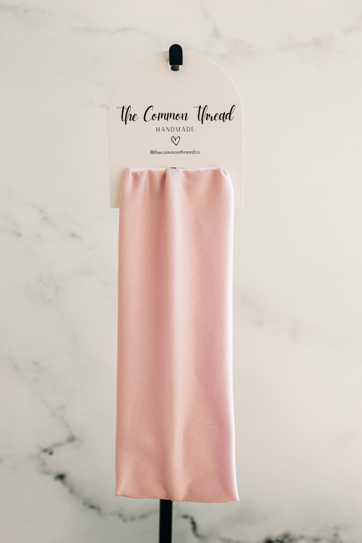 May include: A light pink headband displayed on a white tag with the text "The Common Thread Handmade" and a heart symbol. The headband is made of a soft, silky material.